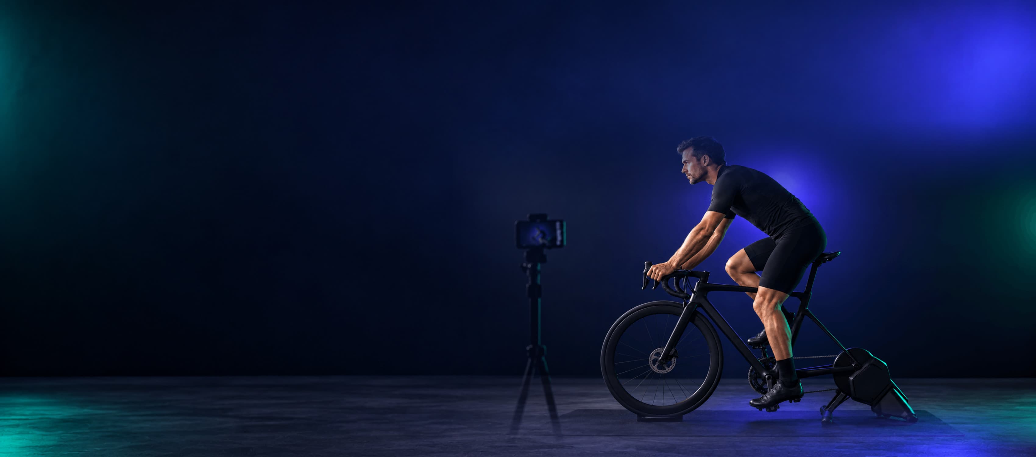 Rider on an indoor trainer being filmed by a phone on a tripod